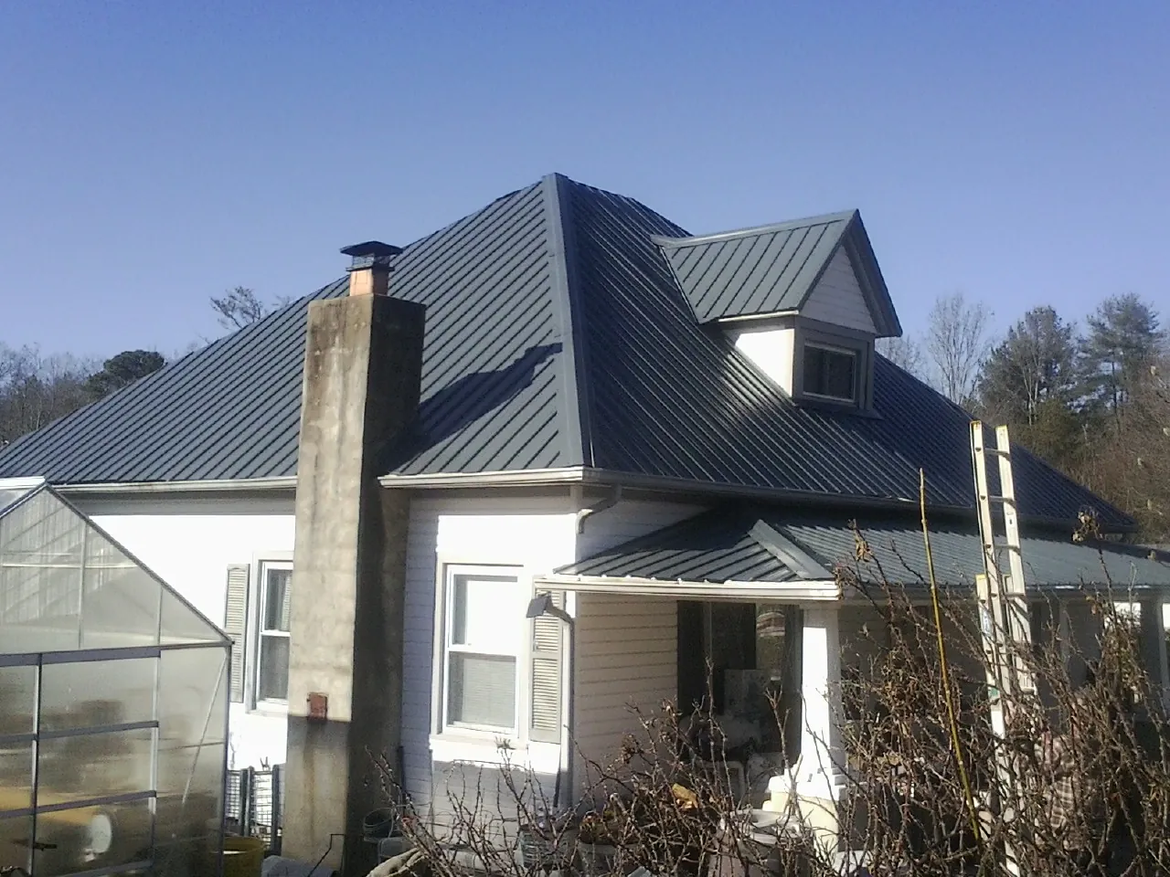 Dark blue standing seam metal roof on a white farmhouse with dormer — Slate & Tile Roof Repair by Roofing Brothers in Rego Park