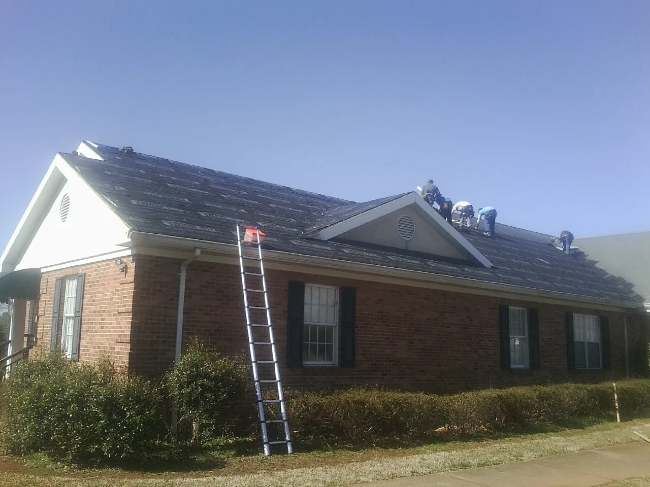 Crew tearing shingles off a brick ranch roof with a ladder set — Emergency Roof Repair work by our crew in Rego Park