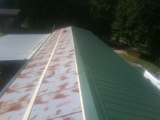 Old rusted panels beside newly installed green metal roofing — Wind Damage Roof Repair by Roofing Brothers in Rego Park