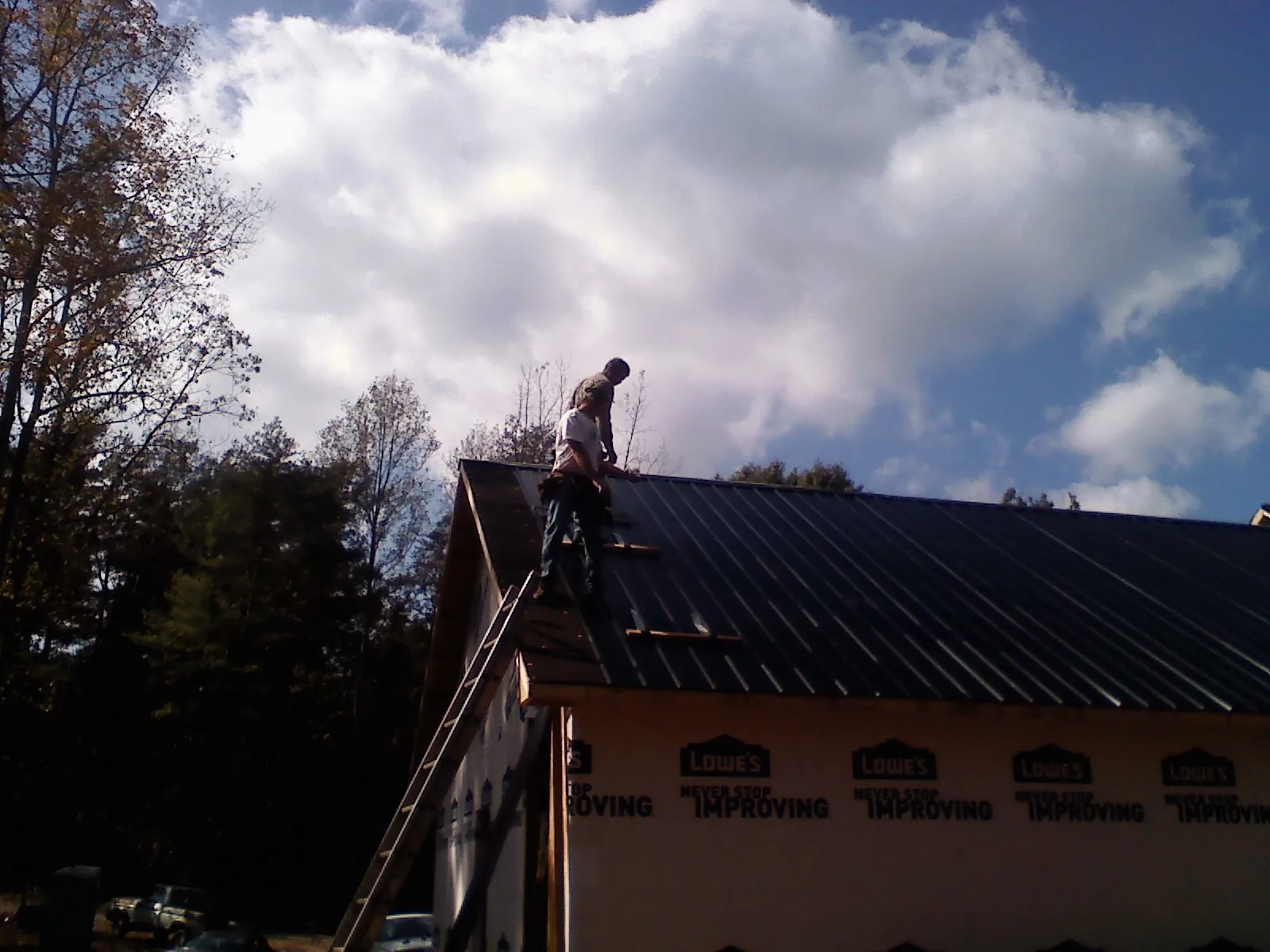 Roofer fastening dark metal panels high against a cloudy sky, from a Roof Inspection job in Rego Park