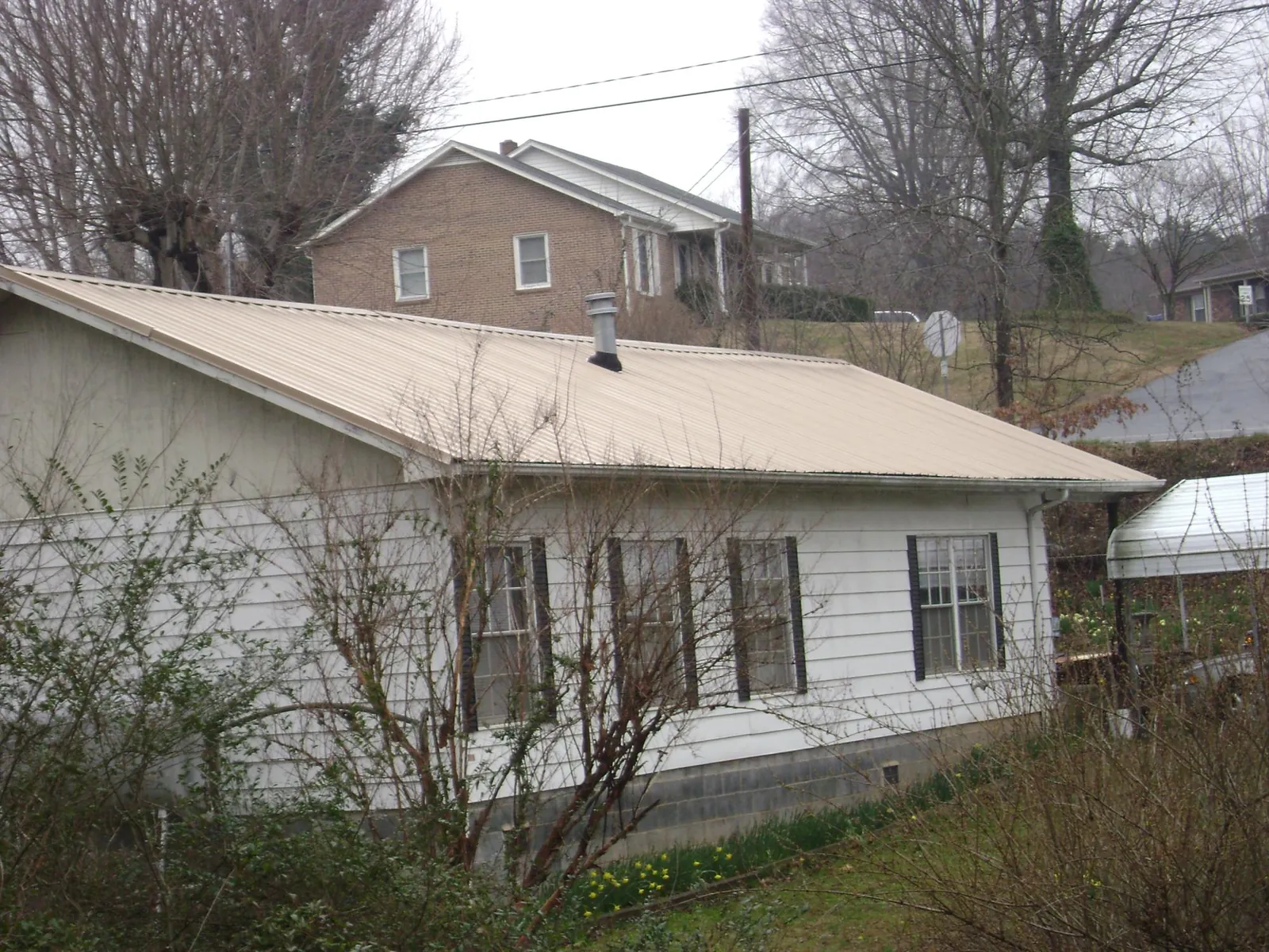Tan metal roof on a white sided house set into a hillside — Commercial Roofing by Roofing Brothers in Rego Park